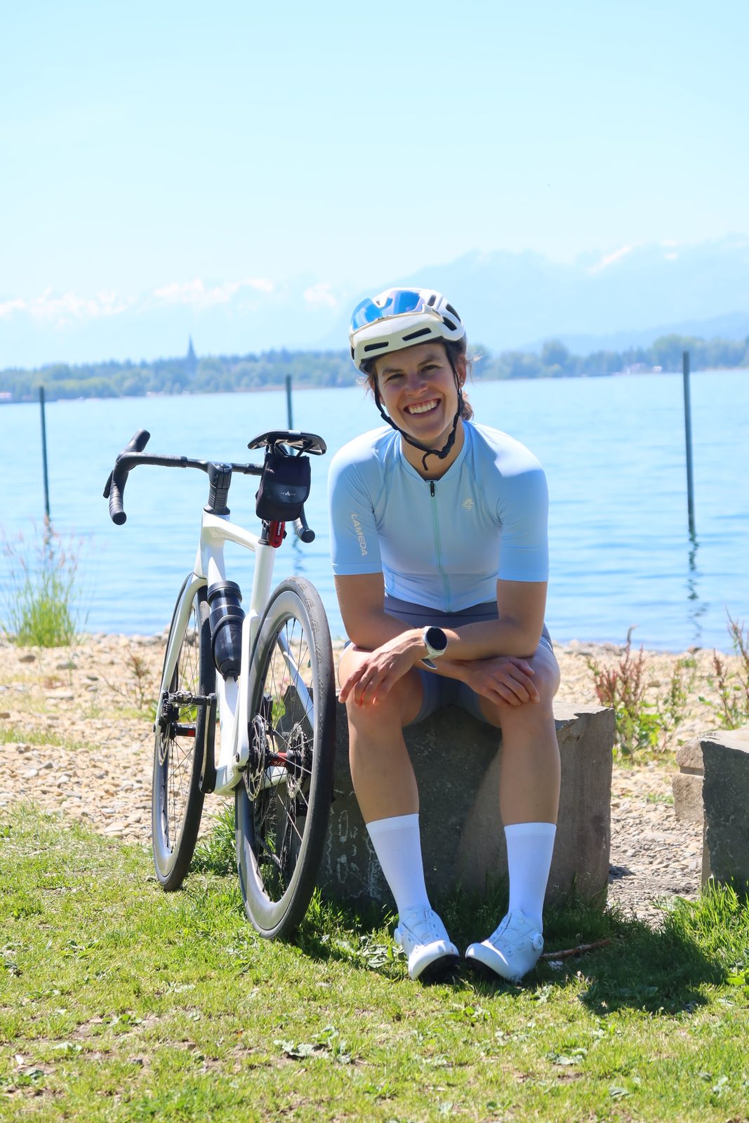 Carmina sitzt näbedem Velo am Wasser und lachet in d'Sunne.